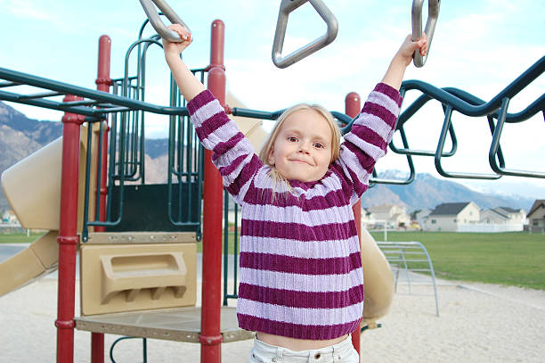 Young blonde girl swinging on the monkey bars stock photo