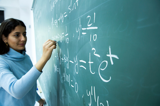 Young and beautiful student studying mathematical formula in front of the blackboard