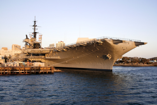 HMAS Adelaide (left) and HMAS Hobart (right) of the Royal Australian Navy docked at Garden Island, Sydney Harbour.  HMAS Adelaide is one of two Canberra Class amphibious assault ships. HMAS Hobart is one of three Hobart Class destroyers. The mast of HMAS Sydney, another Hobart Class destroyer, is visible in the background. This image was taken on a rainy, overcast and windy afternoon on 25 November 2023.