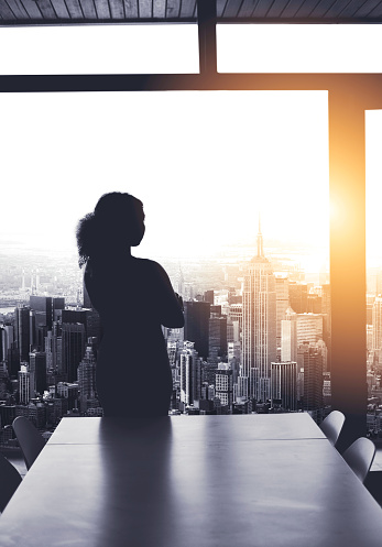 Silhouetted shot of a young businesswoman looking at a cityscape from an office window