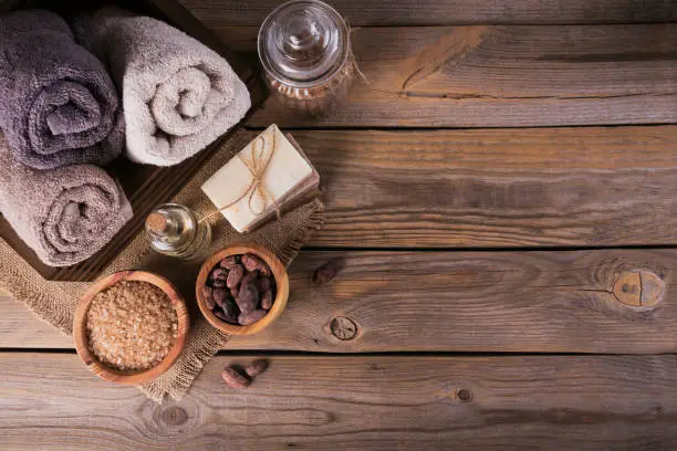 Natural cosmetic oil, sea salt and natural handmade soap with cocoa beans on rustic wooden background. Healthy skin care. SPA concept. Flat lay with space for text.