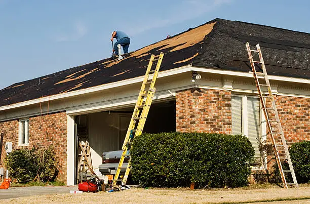 Mexican ethnicity construction male worker is on a rooftop repairing shingles that were destroyed due to an EF2 tornado. With his back turned he is unrecognizable. An EF2 tornado came through this residential neighborhood in Columbus Georgia in the early spring and destroyed many houses and roofs. 