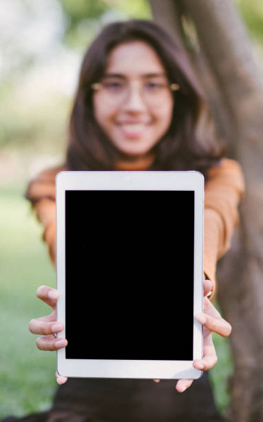 Happy woman showing blank tablet screen over park background. Focus on  tablet.