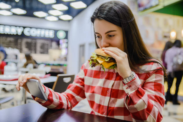 istock woman eat humburger while searfing the phone 912603708