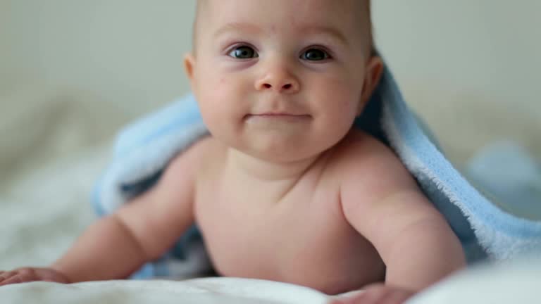 Cute little baby boy, relaxing in bed after bath, smiling happily, daytime