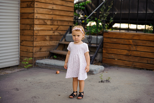 Little girl with a serious look dressed in cute pink dress and black shoes standing outdoors