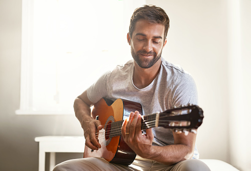 Young asian artist musician playing guitar in white studio. Relaxing with song and music. Asian man having fun playing acoustic guitar singing song