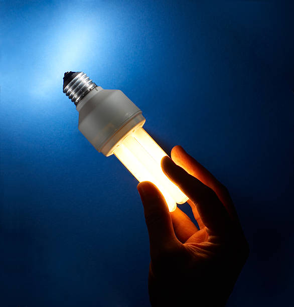 Hand holding an illuminated compact fluorescent light bulb stock photo