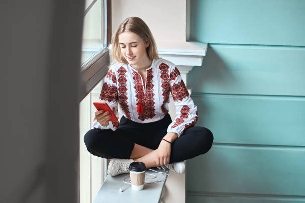 estudiante joven caucásica hermosa usando un vyshyvanka, un ucraniano tradicional bordada camisa comprueba su smartphone en la universidad de - ukrainian culture audio fotografías e imágenes de stock