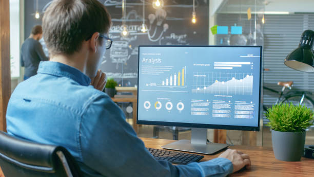 istock Financier Works on a Personal Computer Showing Statistics, Graphs and Charts. In the Background His Coworker and Creative Office. 912636992