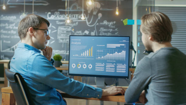 istock Two Office Employees Have Project Related Discussion, on the Desk Stands Personal Computer with Statistics, Graphs and Charts. They Work in the Creative Office Environment. 912637016