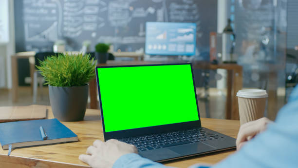 Male Office Worker at His Desk Works on a Laptop with Mock-up Green Screen. Over the Shoulder Close-up Footage. In the Background Creative Office. Male Office Worker at His Desk Works on a Laptop with Mock-up Green Screen. Over the Shoulder Close-up Footage. In the Background Creative Office. looking over shoulder stock pictures, royalty-free photos & images