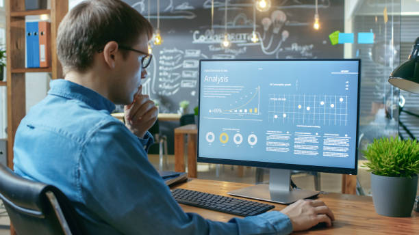 istock Financier Works on a Personal Computer Showing Statistics, Graphs and Charts. In the Background His Coworker and Creative Office. 912637178