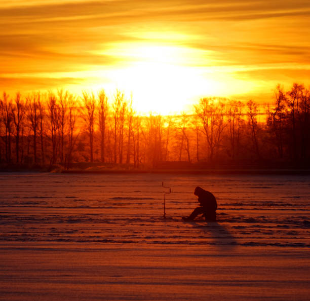 istock fisherman waiting for fish on ice at the sunrise 912644444