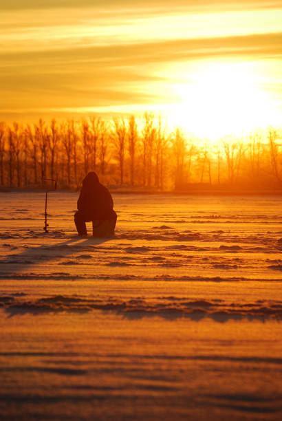 istock fisherman waiting for fish on ice at the sunrise 912644452