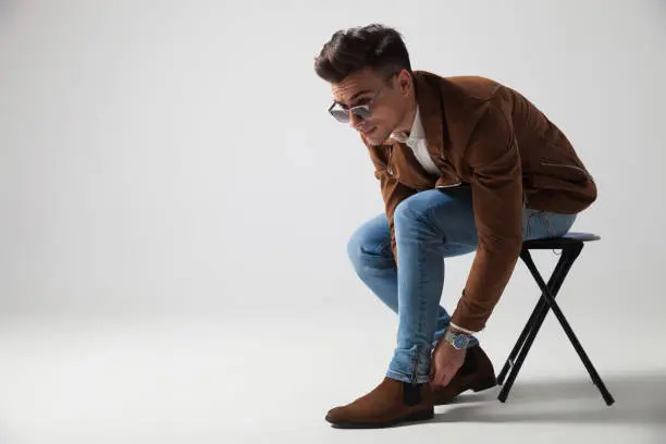 Photo of young casual man sitting and fixing pants while looking away