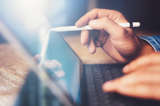 istock Man using contemporary electronic tablet keyboard-dock station while sitting at the wooden table at office.Men using digital stylus pointing to device screen.Blurred background. Horizontal closeup. 912647532