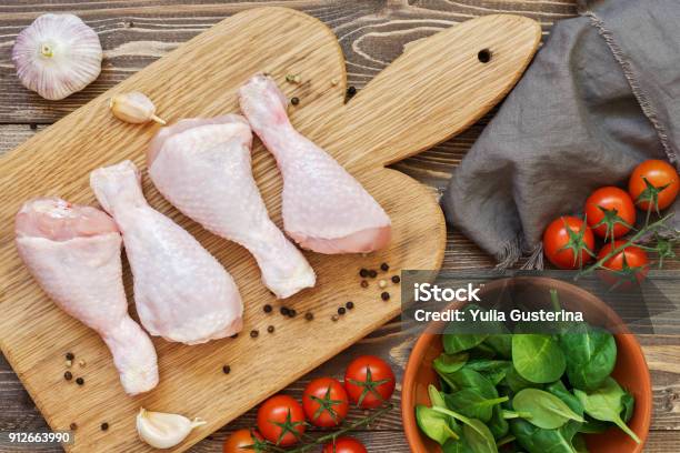 Raw Chicken Drumstick On A Cutting Board Cherry Tomatoes Spinach Garlic Towel On A Wooden Table Top View Stock Photo - Download Image Now