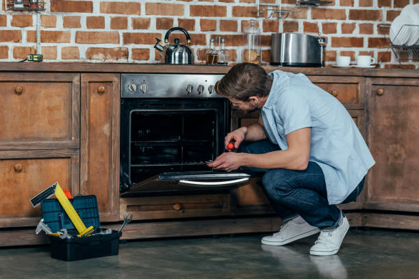 istock casual young man holding screwdriver while repairing oven in kitchen 912671790