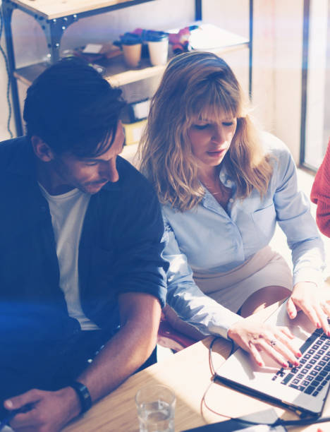 istock Two young coworkers working on notebook computer at sunny office.Woman holding paper documents and pointing on notebook screen. Vertical.Blurred background. 912672874
