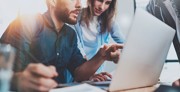 Group of coworkers sitting at the wooden table and working together on new startup project in modern loft office.Horizontal.Blurred background.Cropped