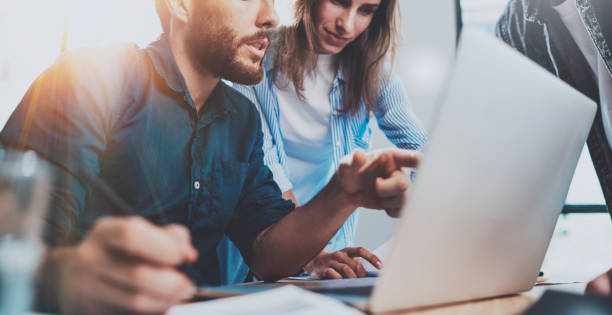 Group of coworkers sitting at the wooden table and working together on new startup project in modern loft office.Horizontal.Blurred background.Cropped. Group of coworkers sitting at the wooden table and working together on new startup project in modern loft office.Horizontal.Blurred background.Cropped financial advisor virtual stock pictures, royalty-free photos & images