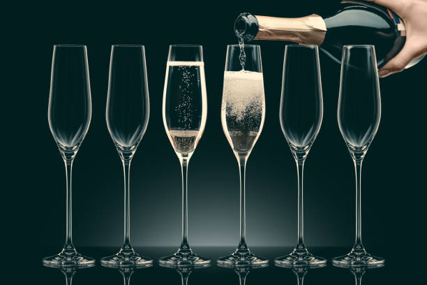 cropped image of woman pouring champagne from bottle into six transparent glasses on black - champagne champagne flute pouring wine imagens e fotografias de stock