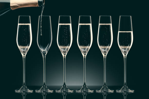 istock pouring champagne from bottle into six transparent glasses on black 912690096