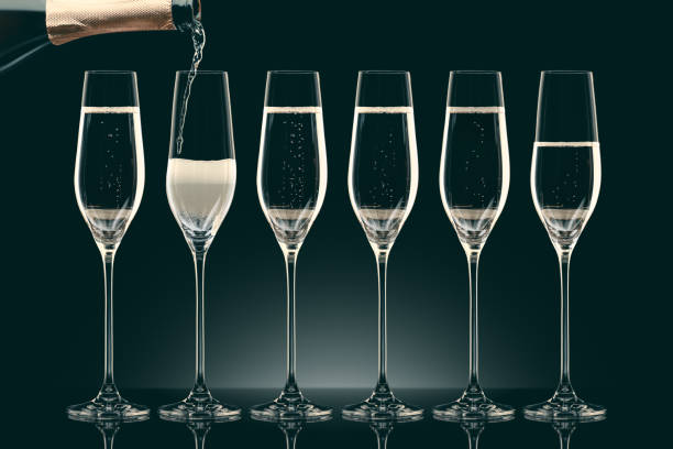 istock pouring champagne from bottle into six transparent glasses on black 912690134