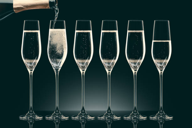 istock pouring champagne from bottle into six transparent glasses on black 912690198