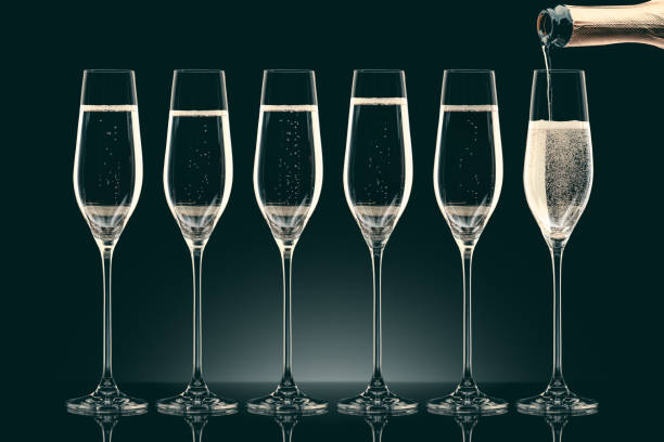 istock pouring champagne from bottle into six transparent glasses on black 912690262