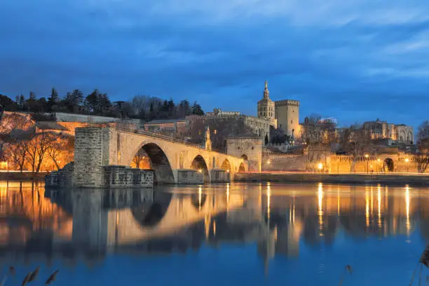 View on Pont d'Avignon 12th century bridge and city skyline reflecting in water at dusk in Avignon, Provence, France