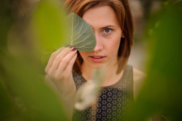 istock Attractive young redhead girl hiding a half of her face with green leaf 912701310