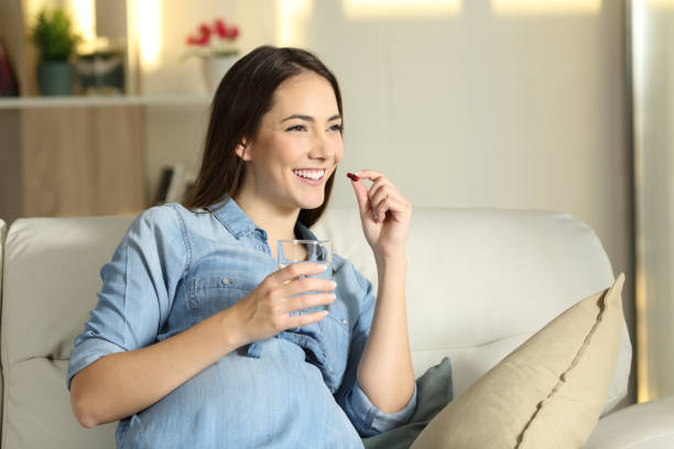 feliz mujer embarazada tomar una pastilla en casa - pill human pregnancy capsule women fotografías e imágenes de stock