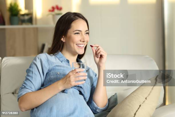 Happy Pregnant Woman Taking A Pill At Home Stock Photo - Download Image Now - Pregnant, Vitamin, Women