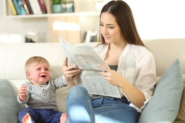 ребенок требует внимания и мать игнорирует его - newspaper reading mother women стоковые фото и изображения