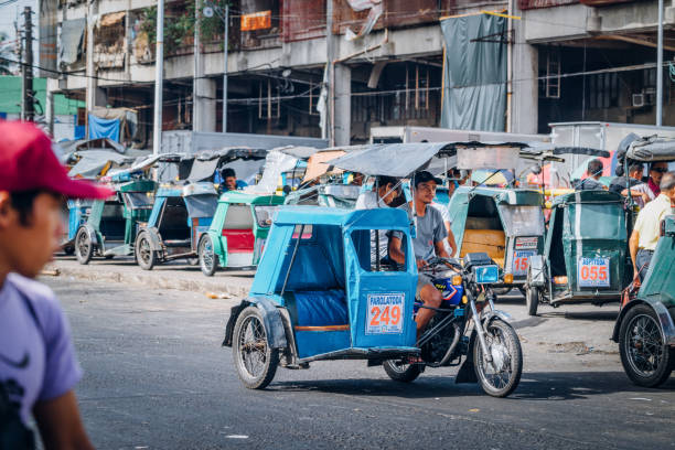 Manila Street Scene with rickshaw driver waiting for clients Manila, Philippines - January  12, 2018: Manila Street Scene with rickshaw driver waiting for clients. Many rickshaw known as a ''Tricycle'' in Metro Manila parking in background. philippines tricycle stock pictures, royalty-free photos & images