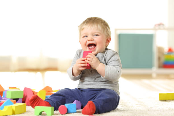 Baby laughing and playing with toys on a carpet Baby laughing and playing with colorful toys sitting on a carpet at home toddlers playing stock pictures, royalty-free photos & images