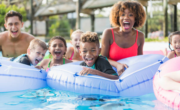 Multi-ethnic children and young adults at water park A group of multi-ethnic children and young adults on the lazy river at a water park, shouting with joy and looking at the camera. The focus is on the mixed race African American and Caucasian 9 year old boy in the center foreground. amusement park photos stock pictures, royalty-free photos & images