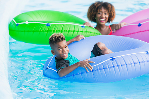 A 9 year old mixed race Caucasian and African American boy having fun at a water park on the lazy river. He is in a blue inflatable innertube, smiling at the camera.