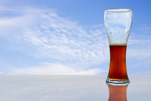 Glass of beer on glass table, bright sky background in summer