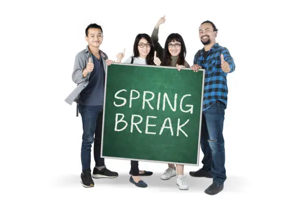 Diversity students showing thumbs up while holding a text of spring break on the chalkboard