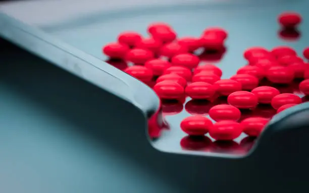 Photo of Macro shot detail of red round sugar coated tablets pills on stainless steel drug tray.