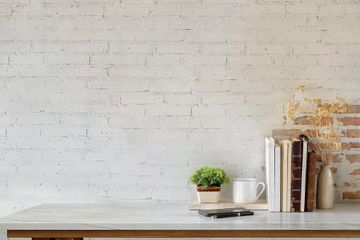 Marble desk with books, coffee mug, mobile phone and plant. Mock up