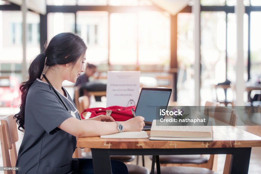 Concentra el médico o la enfermera trabaja en línea con un ordenador portátil sentado en un escritorio en una consulta - Foto de stock de Personal de enfermería libre de derechos