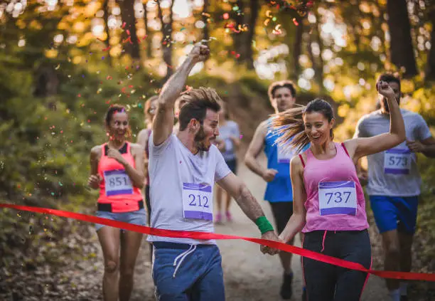 Young smiling couple winning marathon race in the forest and crossing finish line together.