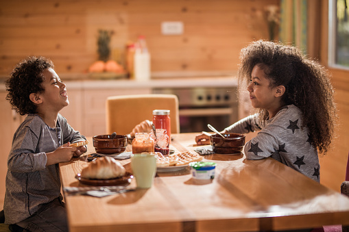 Cute African American kids talking while having breakfast at dining table.