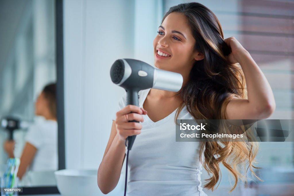 Putting great care into her hair Shot of an attractive young woman blowdrying her hair in the bathroom Hair Dryer Stock Photo