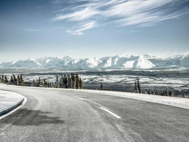 istock winding snowy road leading towards snow mountains 912872606