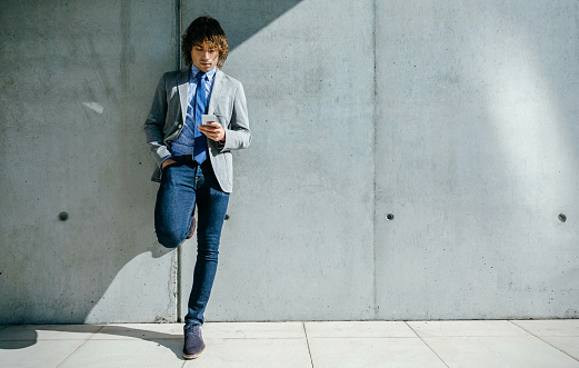 Businessman using mobile leaning on a concrete wall